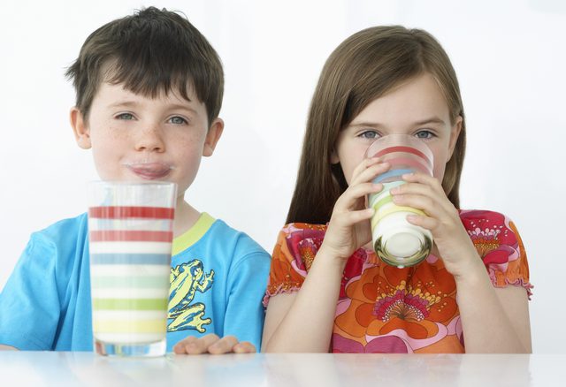 девочка и мальчик пьют молоко из стаканов