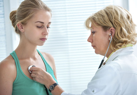 Девушку врач слушает фонендоскопом
